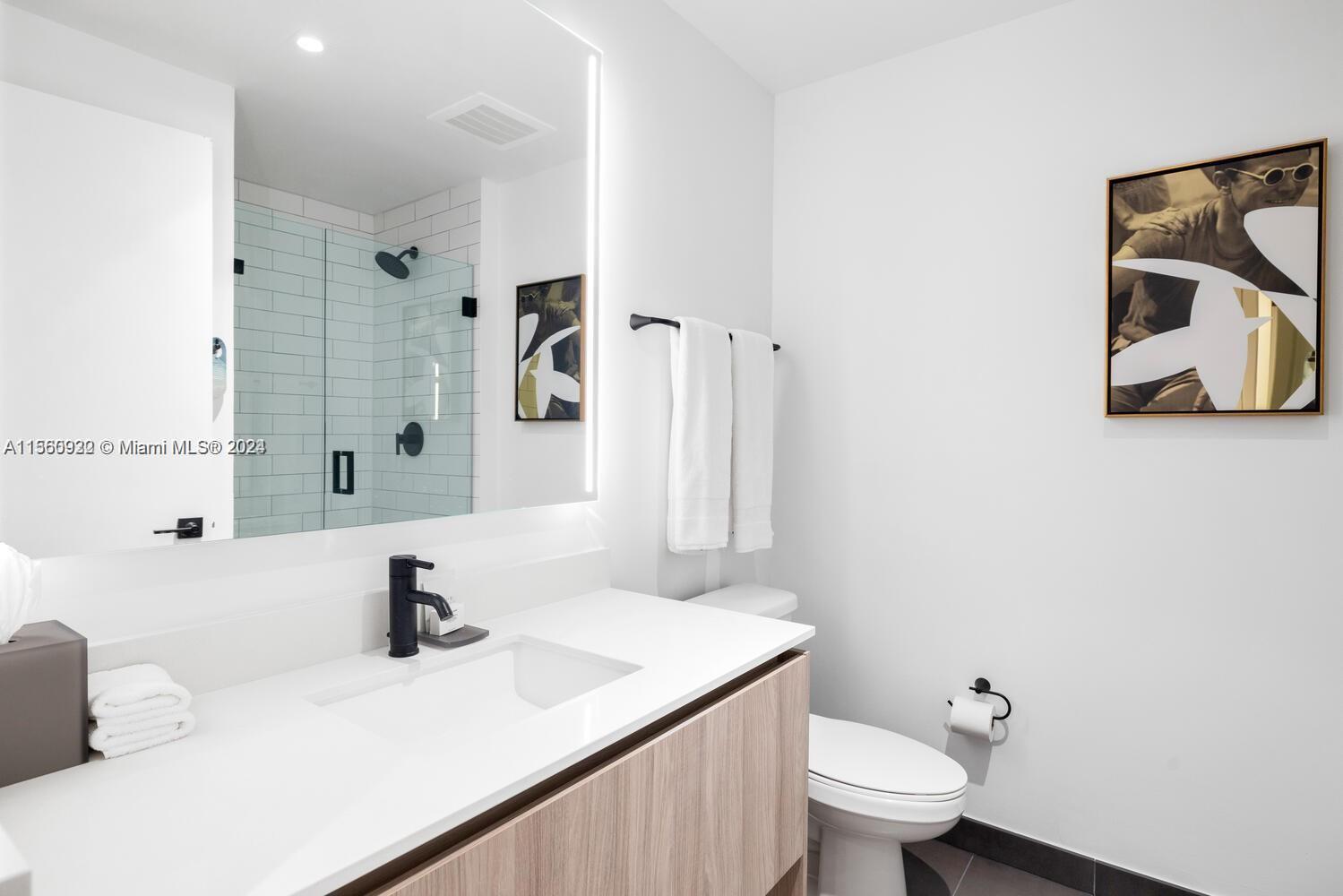 A modern bathroom features a wood vanity, white countertop, black fixtures, and a glass-enclosed shower — 398 NE 5th St # 4708, Miami FL 33132, MIAMI, FL