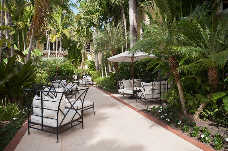 A paved outdoor patio features white cushioned lounge chairs and a large umbrella among tropical plants — 301 Australian Avenue # 306, Palm Beach FL 33480, PALM BEACH, FL