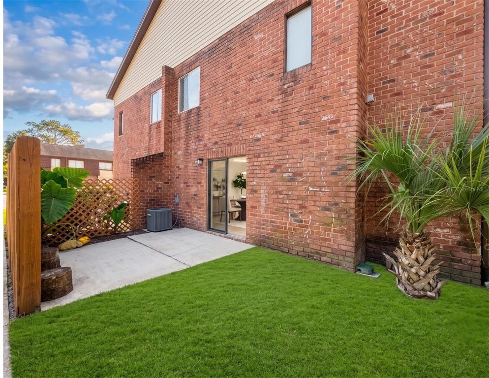 A brick townhouse exterior features a concrete patio, a small lawn, and a palm tree — 5100 PICADILLY CIRCUS UNIT 12, ORLANDO, FL
