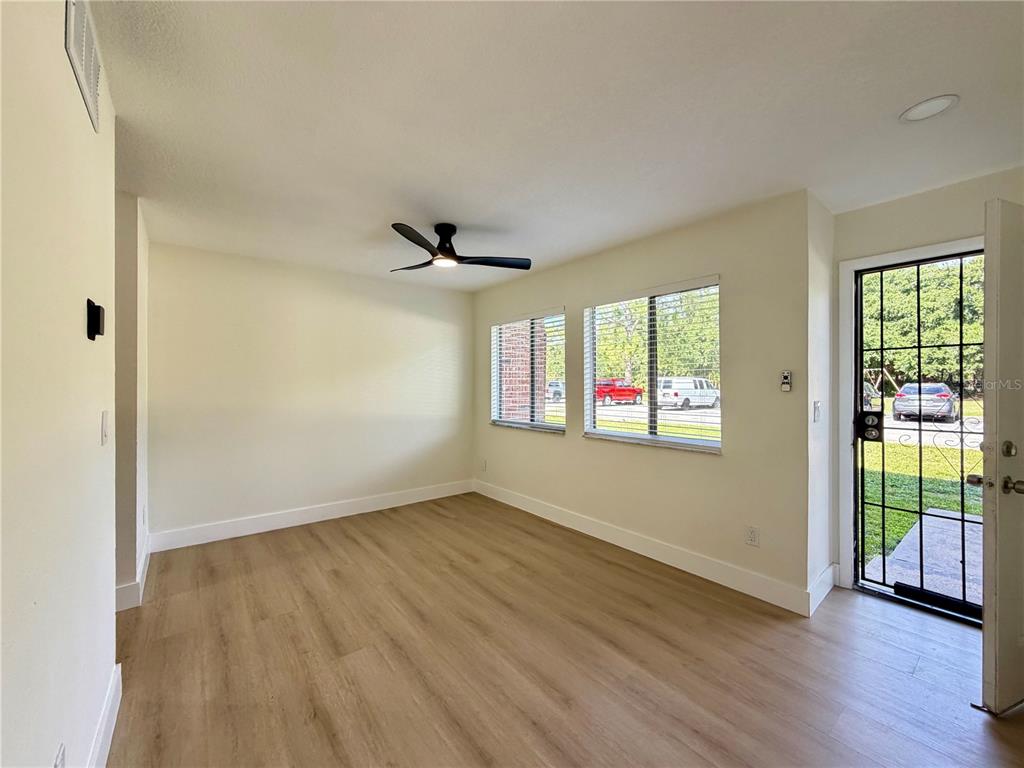 An empty room features light wood-look flooring, a ceiling fan, and a glass-paneled entry door — 5100 PICADILLY CIRCUS UNIT 12, ORLANDO, FL