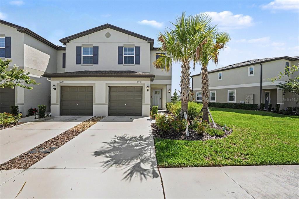 A two-story duplex with two garage doors, a concrete driveway, and a palm tree — 32137 POWDERPUFF MIMOSA DRIVE, SAN ANTONIO, FL