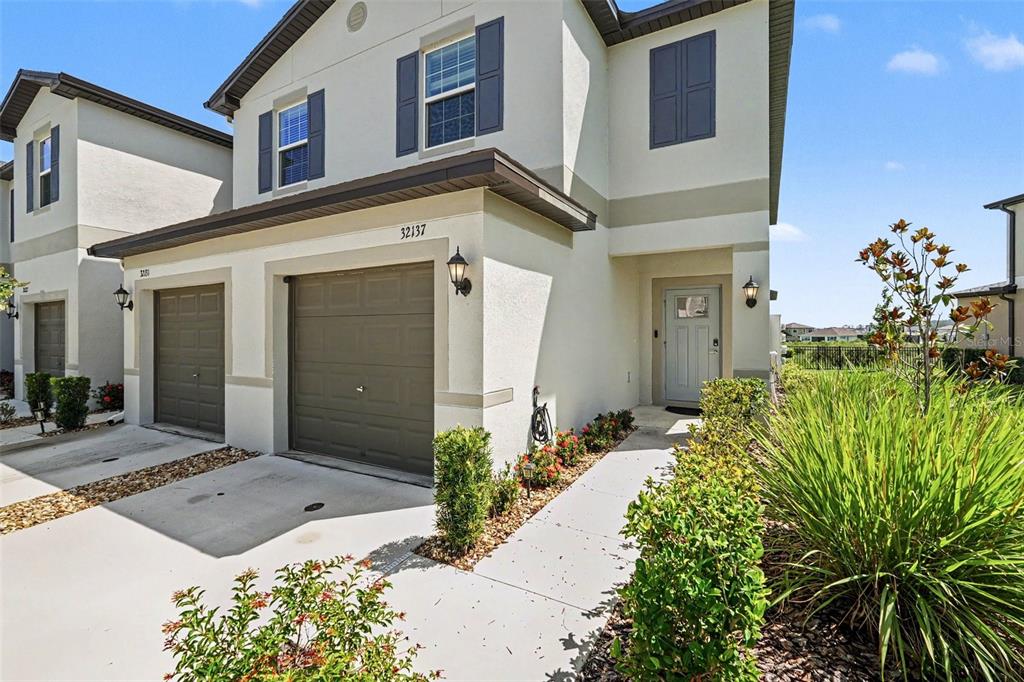 A two-story townhouse with a beige stucco exterior, a single-car garage, and a front walkway — 32137 POWDERPUFF MIMOSA DRIVE, SAN ANTONIO, FL