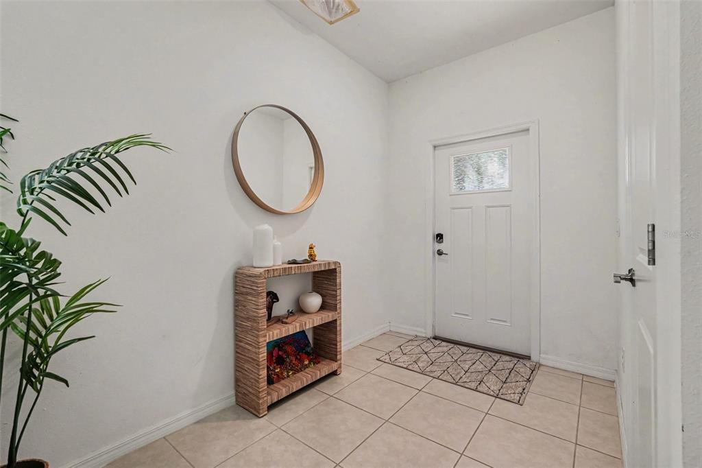 An entryway with tiled floors, a white front door, a round mirror, and a bookshelf — 32137 POWDERPUFF MIMOSA DRIVE, SAN ANTONIO, FL