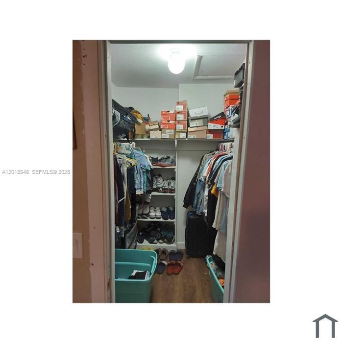 A walk-in closet features built-in shelving, hanging clothes, and storage bins on the floor — 207 NE 141st St # 4, Miami FL 33161, MIAMI, FL