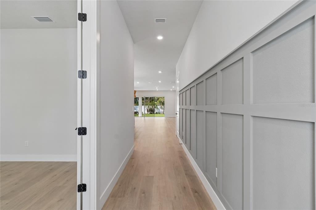 A hallway with light wood flooring leads to an open living area with glass doors — 3711 W DE LEON STREET, TAMPA, FL