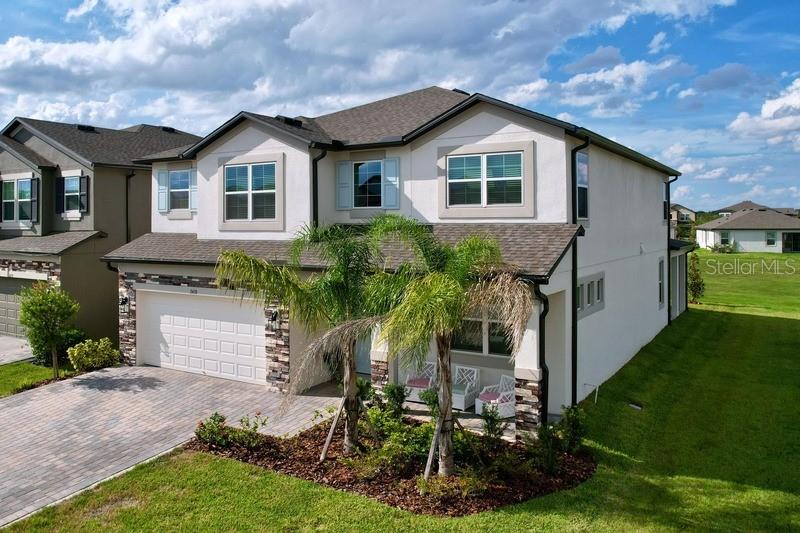 A two-story suburban house features a stone-accented facade, a paved driveway, and palm trees — 2450 SUNNY PEBBLE LOOP, ZEPHYRHILLS, FL