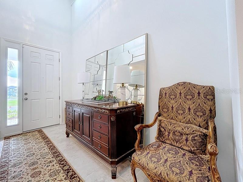 A foyer features a dark wood dresser, large mirrors, and an ornate patterned armchair — 2450 SUNNY PEBBLE LOOP, ZEPHYRHILLS, FL