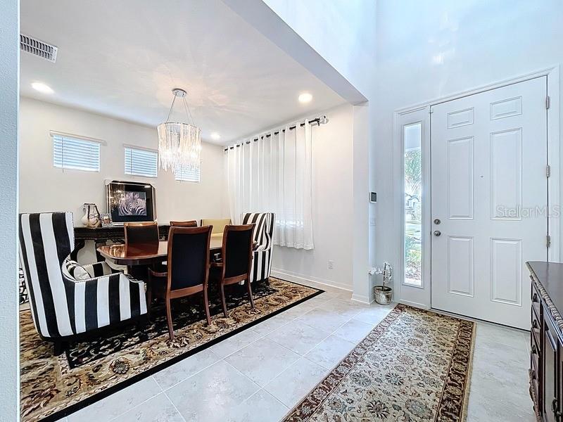 A dining room with a chandelier, striped chairs, and a front entryway with a door — 2450 SUNNY PEBBLE LOOP, ZEPHYRHILLS, FL