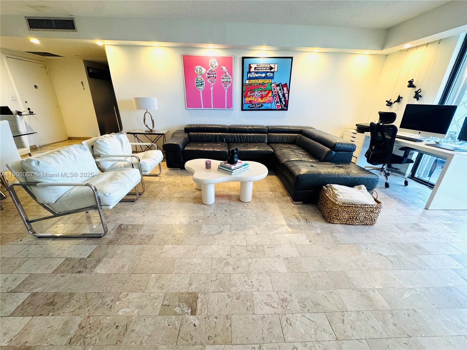 A living room features a black sectional sofa, two white chairs, and colorful wall art — 600 Three Islands Blvd # 1206, Hallandale Beach FL 33009, HALLANDALE BEACH, FL