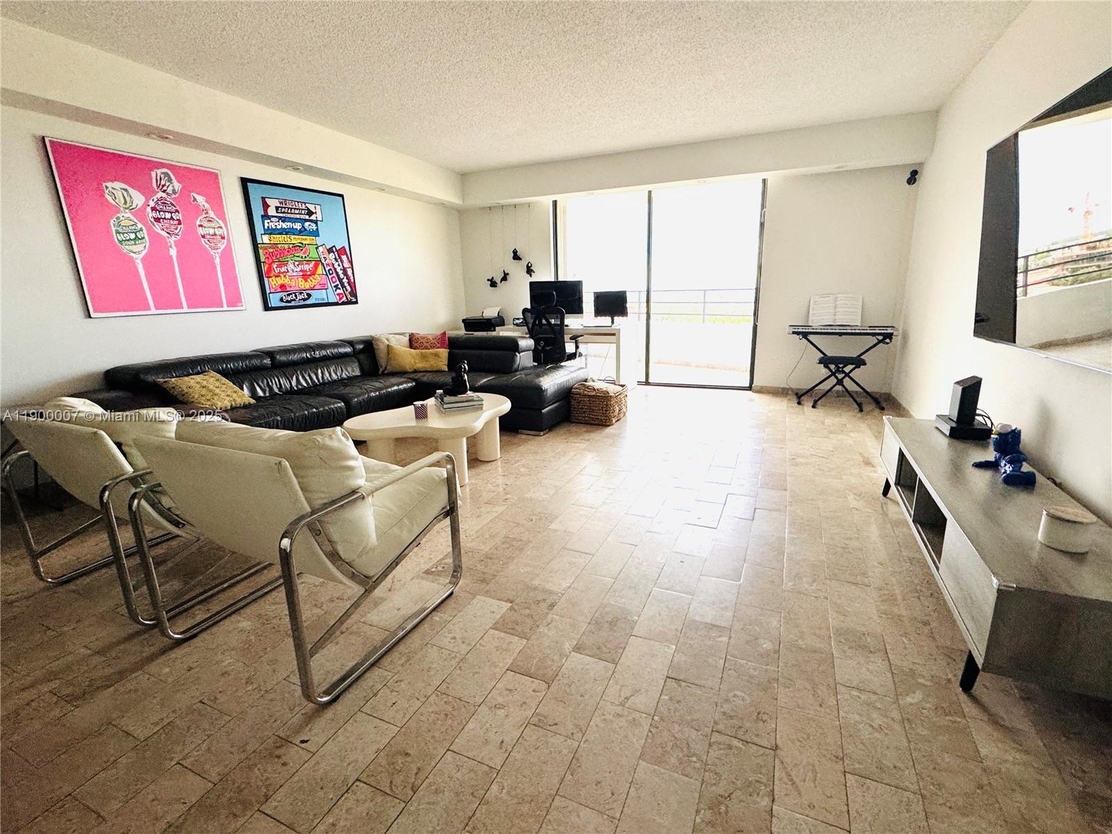 A living room features a black sectional sofa, white chairs, tile floors, and large windows — 600 Three Islands Blvd # 1206, Hallandale Beach FL 33009, HALLANDALE BEACH, FL
