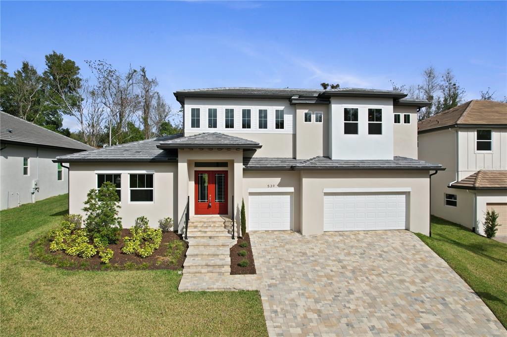 A two-story house with a beige stucco exterior, red double front doors, and a paved driveway — 539 SANCTUARY GOLF PLACE, APOPKA, FL