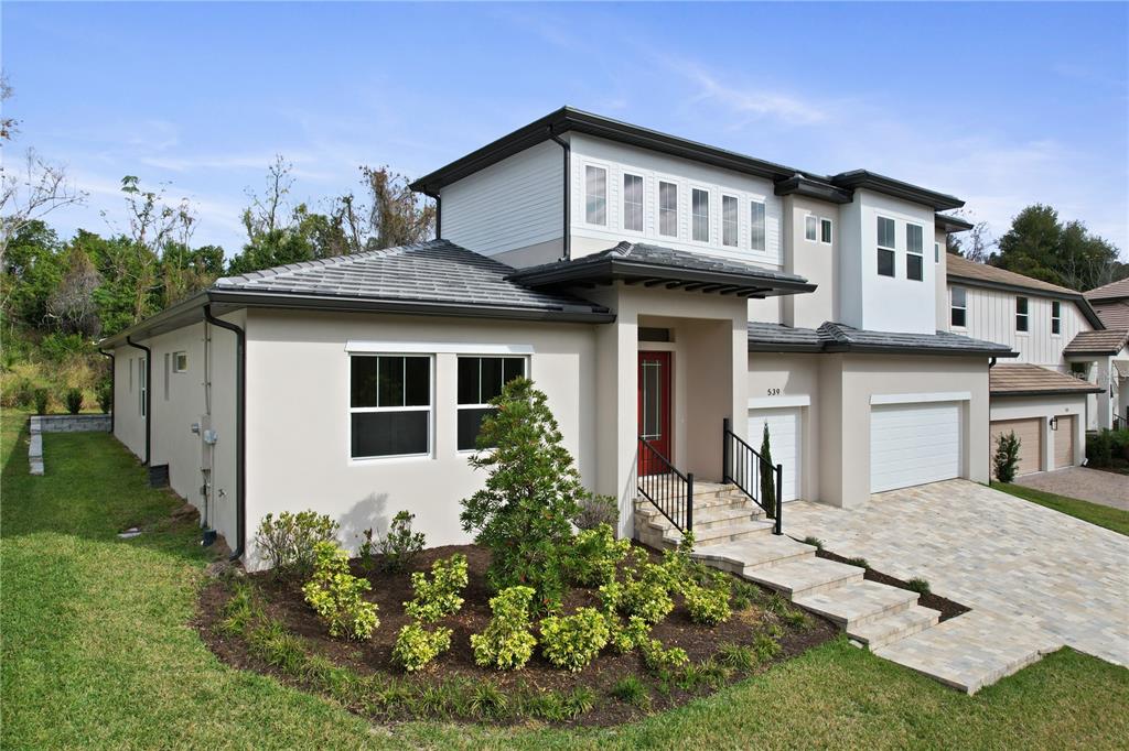 A two-story house with a beige stucco exterior, a red front door, and a stone driveway — 539 SANCTUARY GOLF PLACE, APOPKA, FL