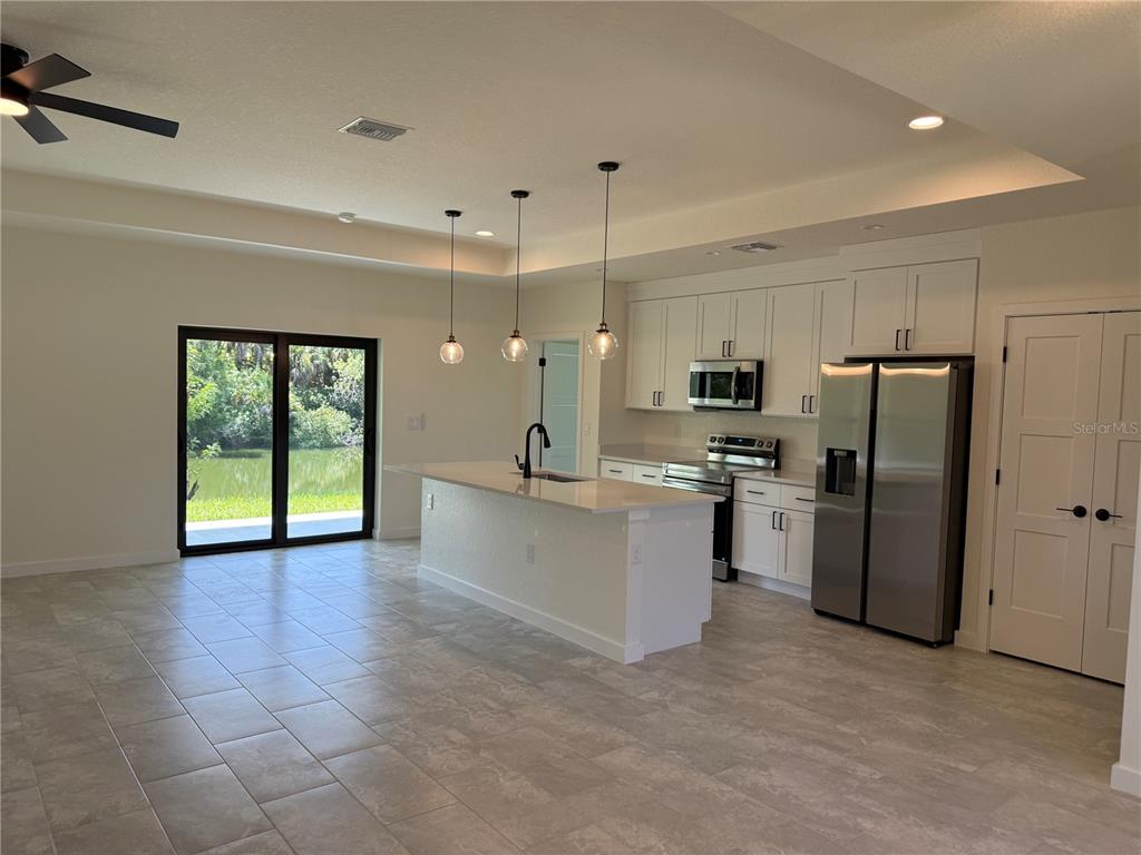 A modern kitchen features white cabinets, stainless steel appliances, and an island with pendant lights — 2646 SADNET LANE, NORTH PORT, FL
