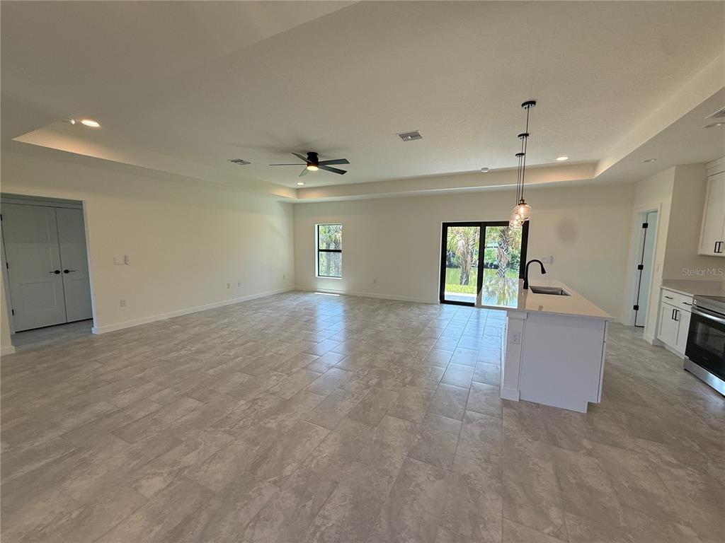 An open-concept kitchen and living area features light tile flooring, white cabinetry, and sliding glass doors — 2646 SADNET LANE, NORTH PORT, FL