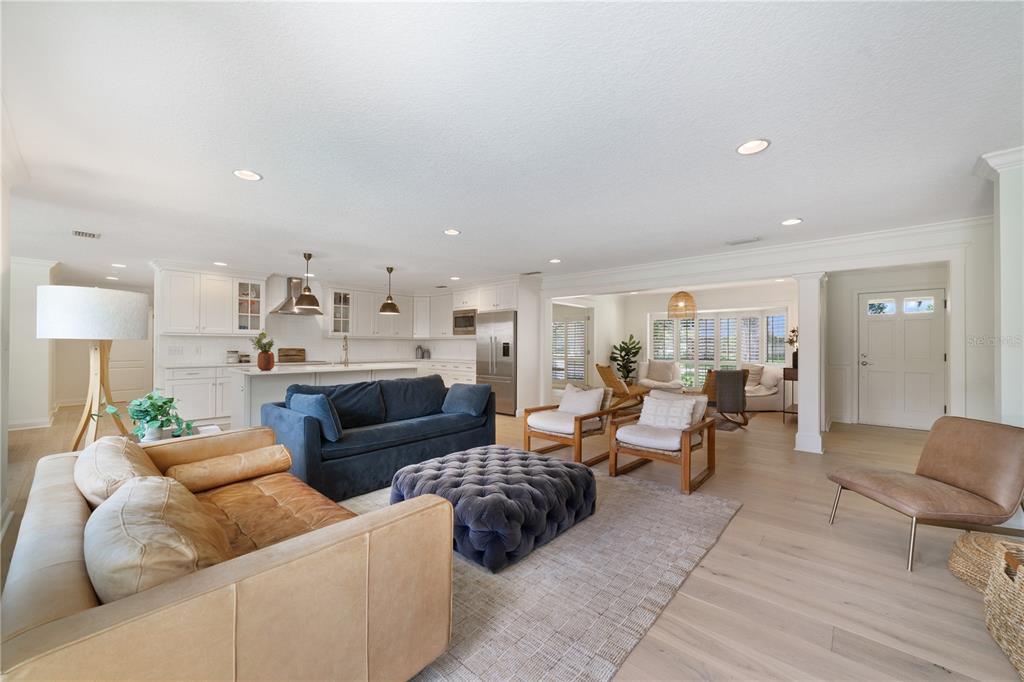 An open-concept living room and kitchen featuring light wood floors, white cabinetry, and varied seating — 1615 KING ARTHUR CIRCLE, MAITLAND, FL