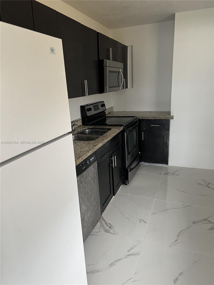 This kitchen features dark cabinets, granite countertops, stainless steel appliances, and white marble-patterned tile flooring — 4809 SW 25th St, West Park FL 33023, WEST PARK, FL