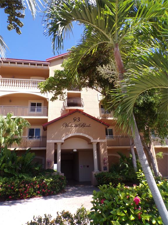 A multi-story tan stucco apartment building with balconies and a palm tree in the foreground — 93 VIVANTE BOULEVARD UNIT 9333, PUNTA GORDA, FL