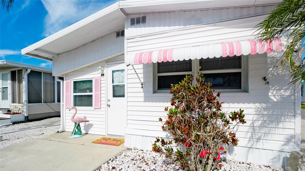 The exterior of a white mobile home features a pink-striped awning and a flamingo statue — 10315 CORTEZ ROAD W UNIT 31-1, BRADENTON, FL