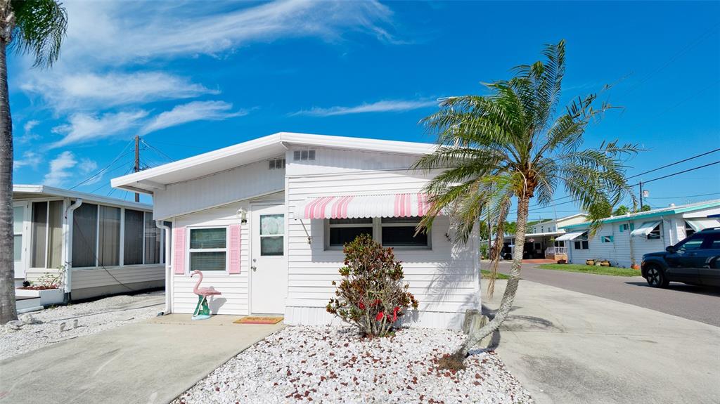 A white mobile home features pink shutters, a striped awning, and a small palm tree — 10315 CORTEZ ROAD W UNIT 31-1, BRADENTON, FL