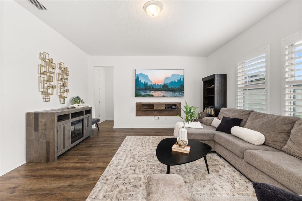 A living room features a grey sectional sofa, a wall-mounted television, and wood-look flooring — 2933 DEERBERRY LANE, CLERMONT, FL