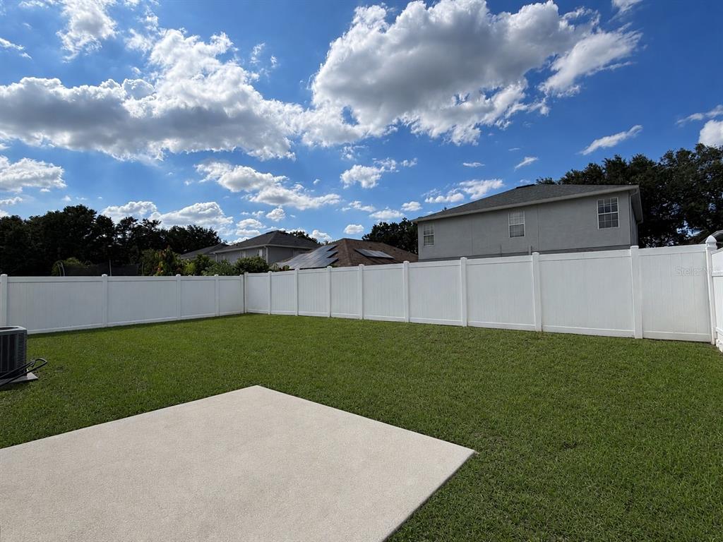 A backyard with a concrete patio, green lawn, and a white vinyl privacy fence — 13508 BLUE SUNFISH COURT, RIVERVIEW, FL