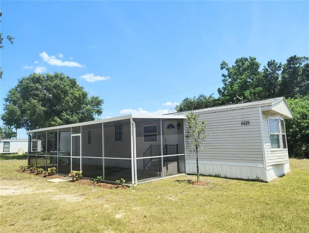 A single-story mobile home features a large screened-in porch and light-colored horizontal siding — 6619 ORANGE BLOSSOM LANE, PUNTA GORDA, FL