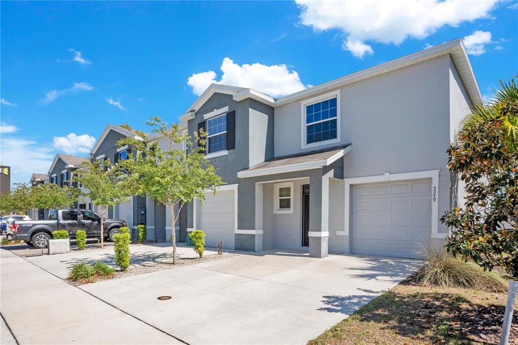 A two-story townhouse with a gray stucco exterior, a single-car garage, and a concrete driveway — 5359 PINECONE COURT, WILDWOOD, FL