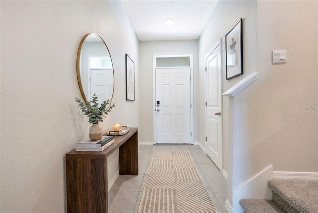 A bright entryway features a wooden console table, a round mirror, and a patterned rug — 5359 PINECONE COURT, WILDWOOD, FL