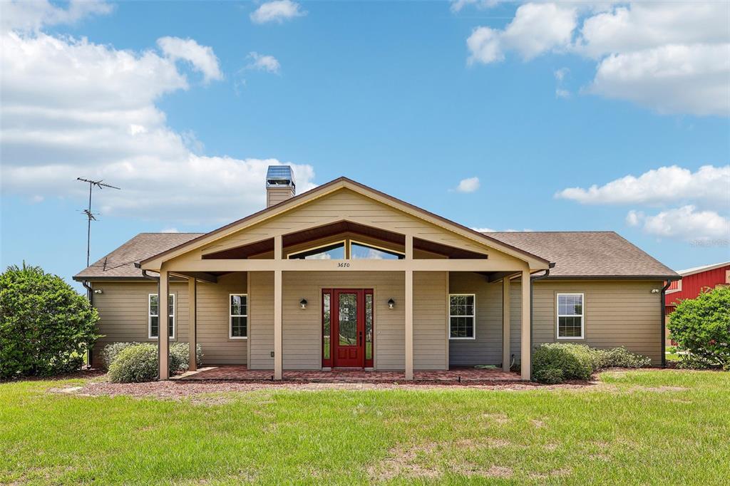 A one-story house with tan siding, a red front door, and a covered brick porch — 3670 LAKE HATCHINEHA ROAD, HAINES CITY, FL