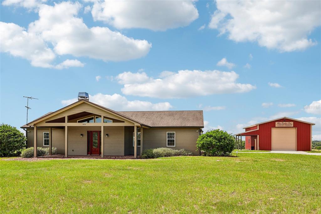 A tan house with a covered porch and a red metal barn on a grassy lot — 3670 LAKE HATCHINEHA ROAD, HAINES CITY, FL