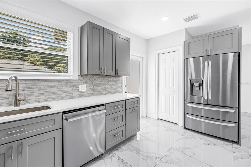 A modern kitchen features gray cabinets, stainless steel appliances, white countertops, and marble-patterned tile floors — 1827 16TH STREET S, ST PETERSBURG, FL