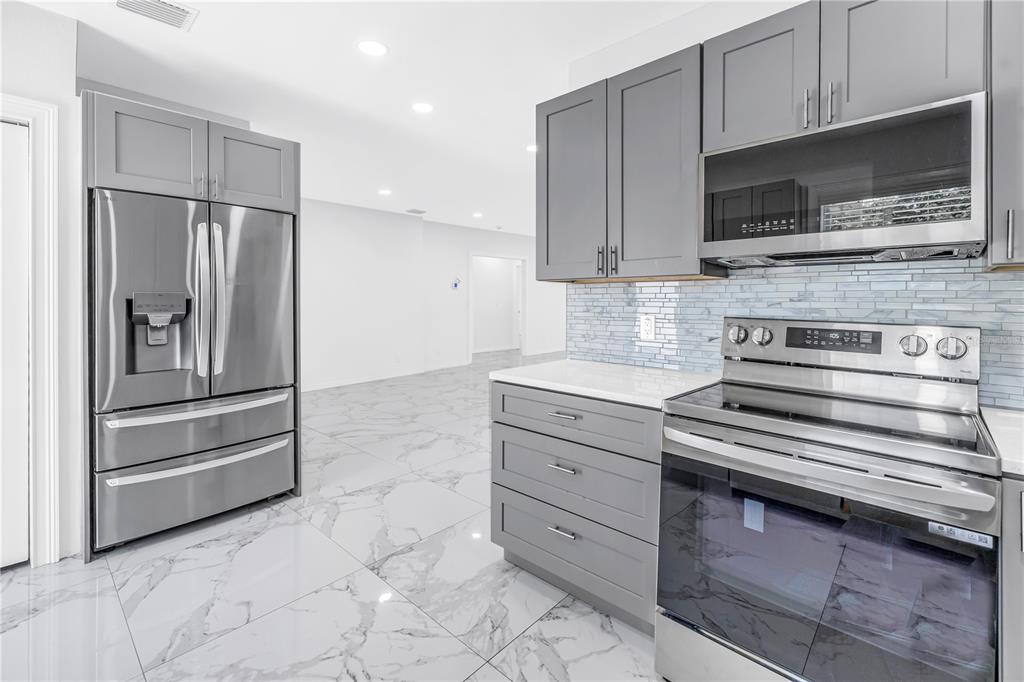 A modern kitchen features gray cabinets, stainless steel appliances, and white marble-patterned tile flooring — 1827 16TH STREET S, ST PETERSBURG, FL