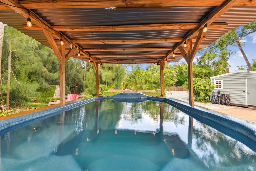 An above-ground pool sits under a wooden pergola with string lights in a backyard setting — 5909 MOHR ROAD, TAMPA, FL