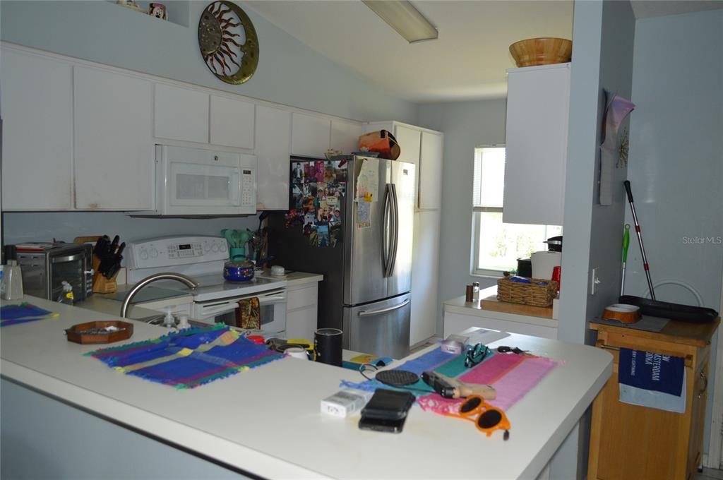 A kitchen features white cabinets, stainless steel appliances, and a peninsula counter with colorful mats — 2308 PALM AVENUE, SEFFNER, FL