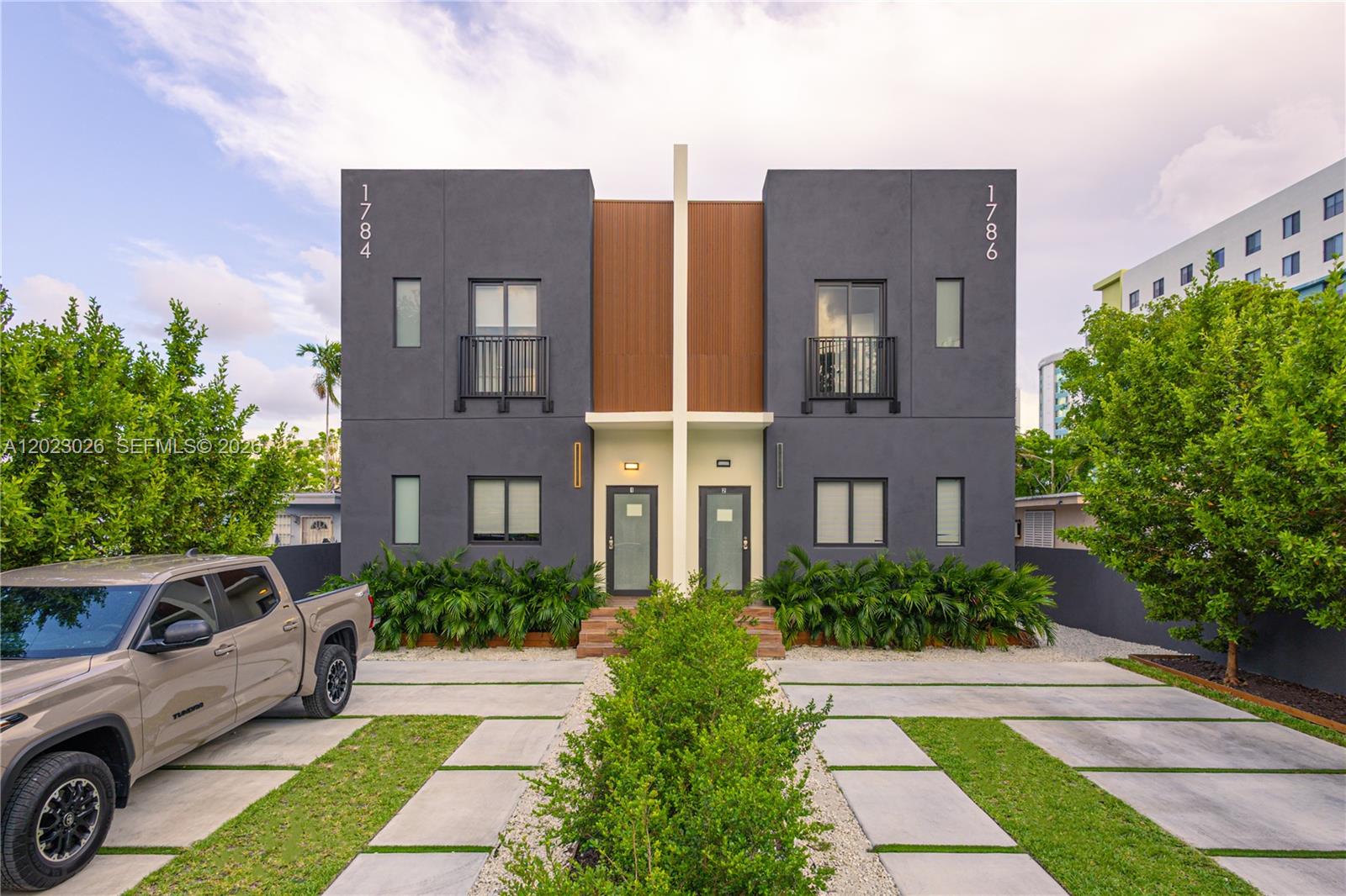 A modern two-story duplex with gray stucco walls, wood accents, and a concrete driveway — 1784 & 1786 NW 31st St, Miami FL 33142, MIAMI, FL