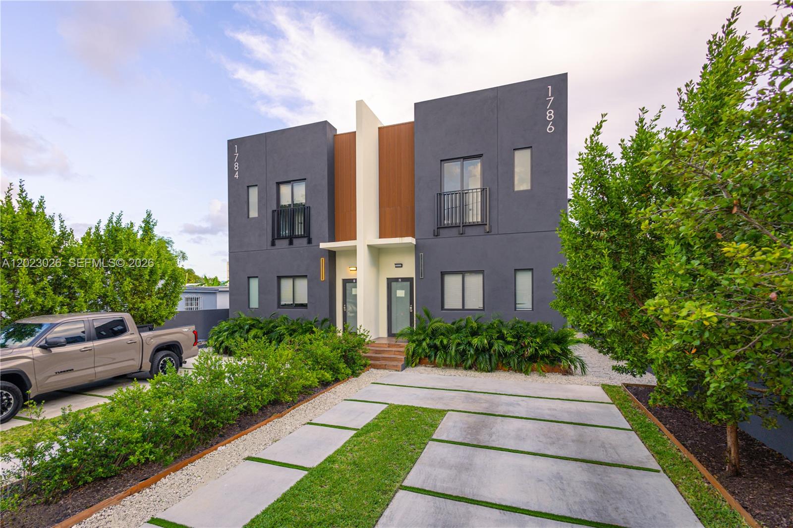 A modern two-story duplex with dark gray stucco, wood accents, and a concrete driveway — 1784 & 1786 NW 31st St, Miami FL 33142, MIAMI, FL