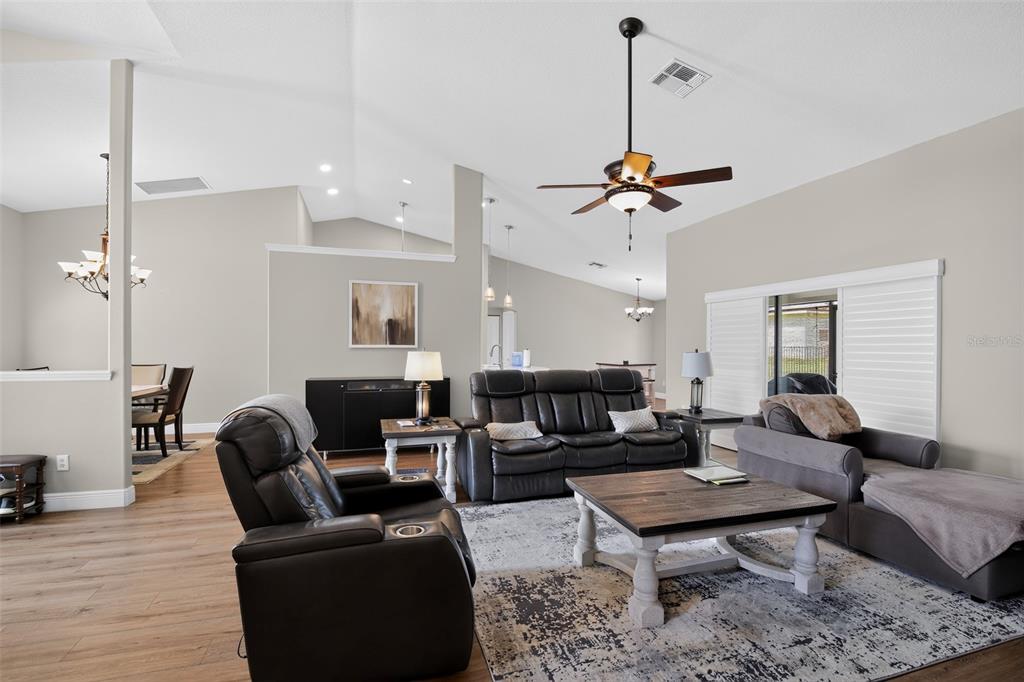 A living room features a vaulted ceiling, dark leather furniture, and wood-look flooring — 6535 SW 51ST TERRACE, OCALA, FL