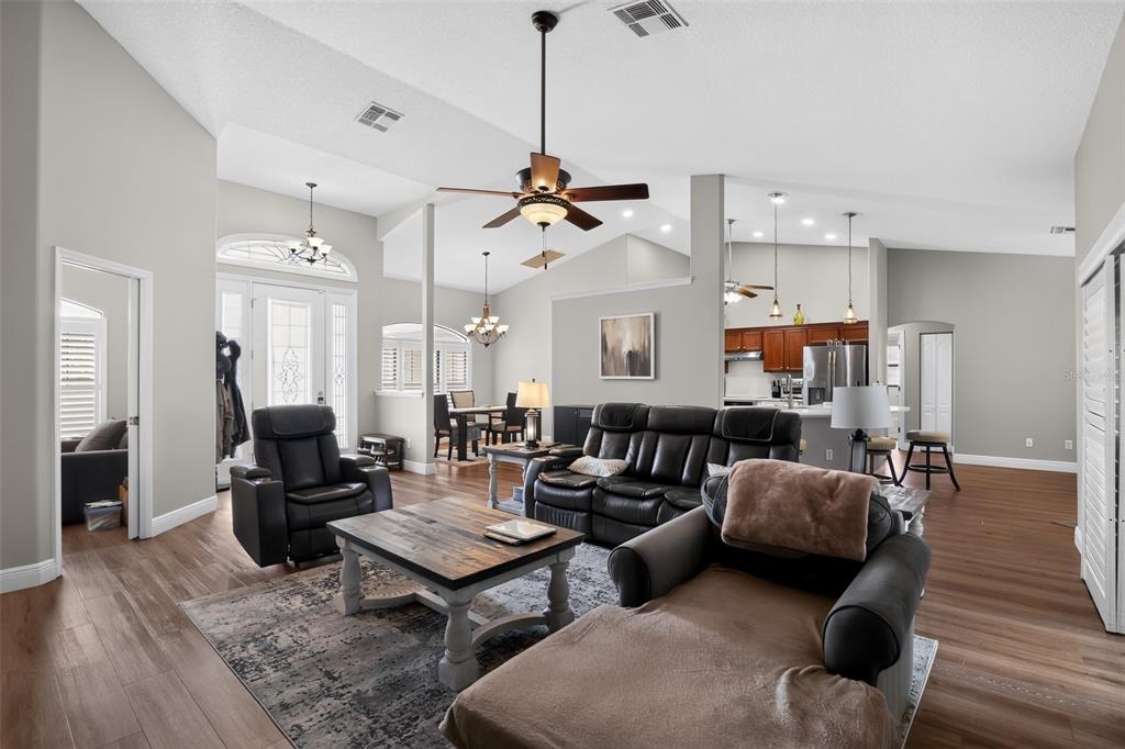 A living room with wood-look flooring, a ceiling fan, and an open kitchen in the background — 6535 SW 51ST TERRACE, OCALA, FL