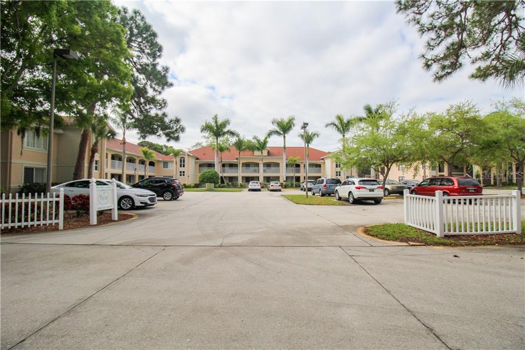 A parking lot sits in front of a multi-story apartment complex with palm trees — 4457 45TH AVENUE W UNIT 110, BRADENTON, FL