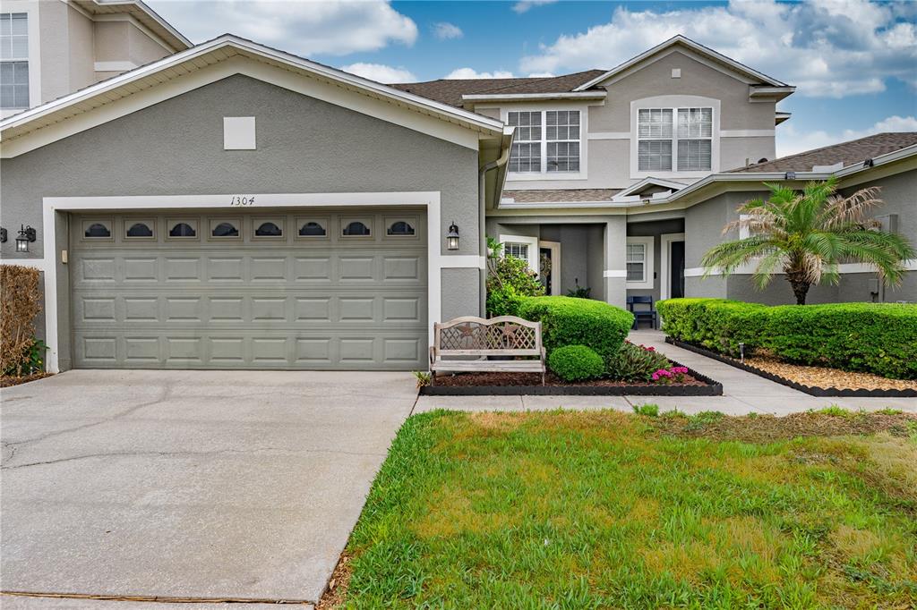 A two-story suburban house features a gray stucco exterior, a two-car garage, and landscaping — 1304 SANDSTONE RUN, SANFORD, FL