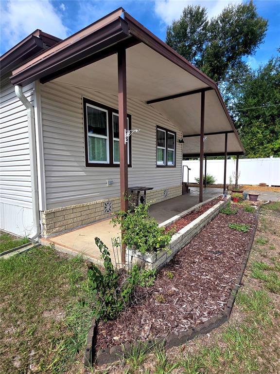 The exterior of a house features light-colored siding, a covered porch, and a landscaped garden bed — 37408 MARTA AVENUE, ZEPHYRHILLS, FL