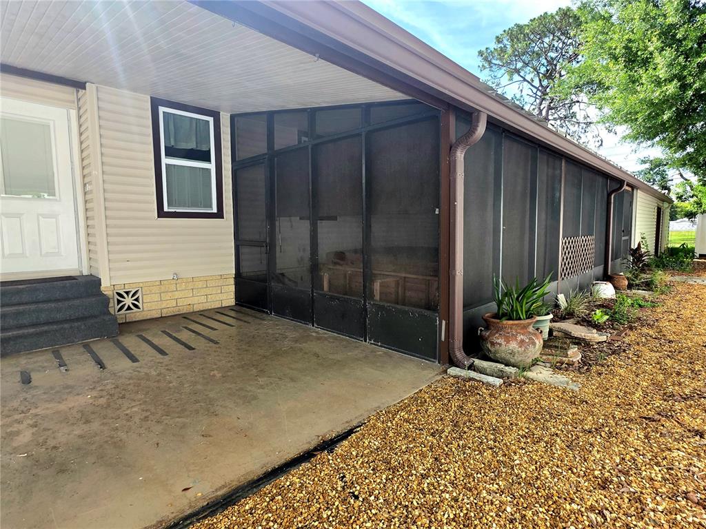 A concrete patio sits beside a screened-in porch with beige siding and a white door — 37408 MARTA AVENUE, ZEPHYRHILLS, FL