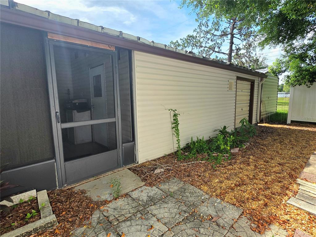 A side view of a mobile home with beige siding, a screen door, and gravel landscaping — 37408 MARTA AVENUE, ZEPHYRHILLS, FL