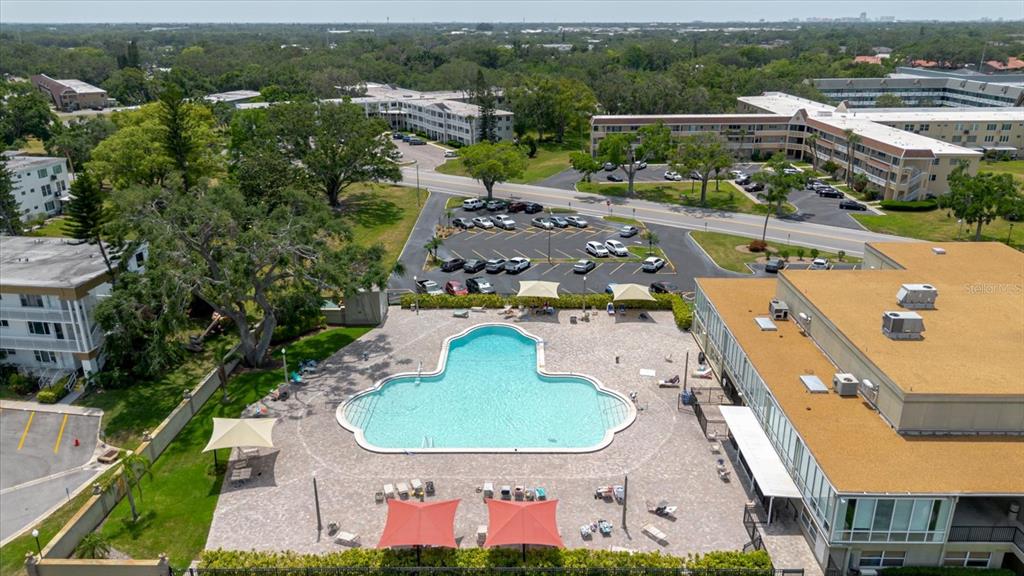 An aerial view shows a swimming pool with a deck, lounge chairs, and nearby buildings — 2295 AMERICUS BOULEVARD E UNIT 59, CLEARWATER, FL