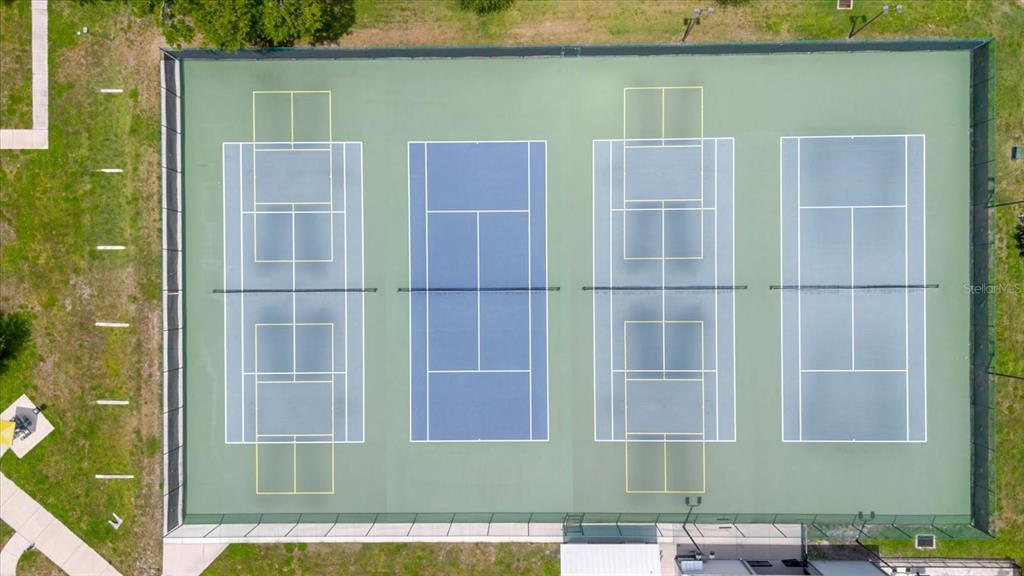 An aerial view shows four tennis courts enclosed by a fence on a grassy lot — 2295 AMERICUS BOULEVARD E UNIT 59, CLEARWATER, FL