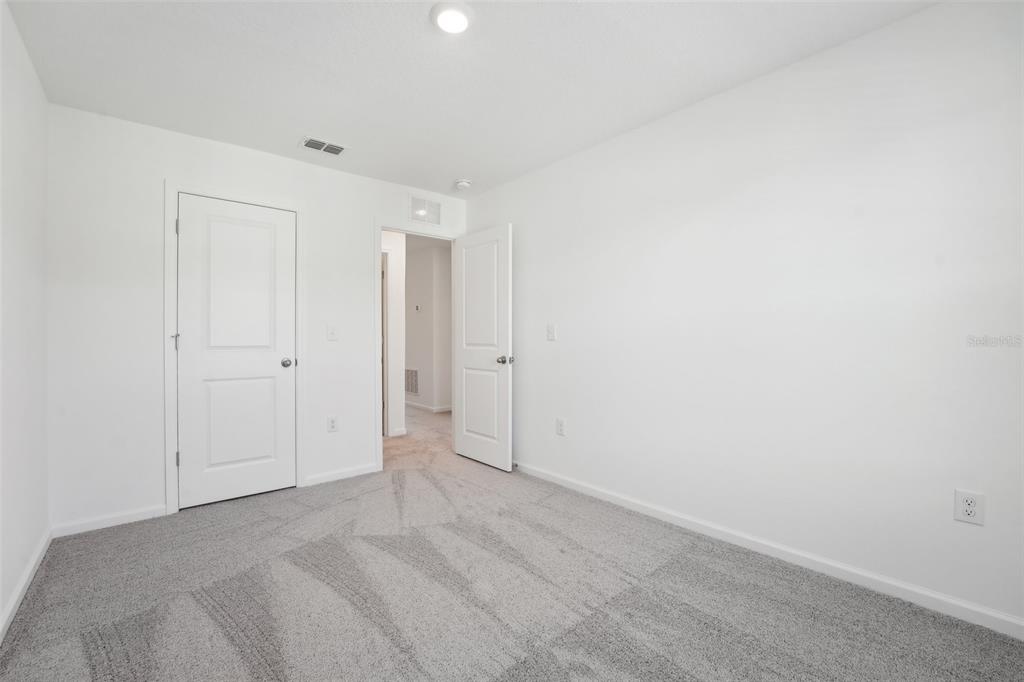 An empty bedroom features white walls, gray carpet, and two white interior doors — 14848 LUCCA WAY, DADE CITY, FL