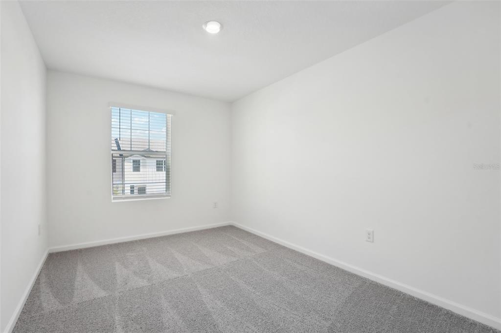 An empty bedroom features white walls, gray carpet, and a single window with blinds — 14848 LUCCA WAY, DADE CITY, FL