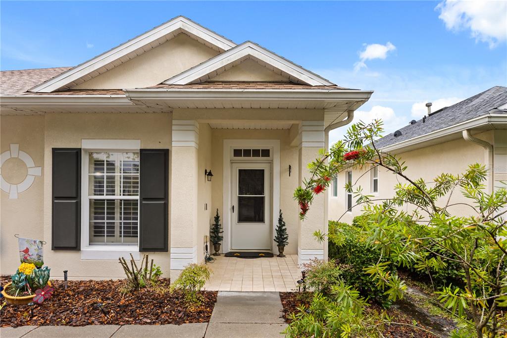 A beige house exterior features a covered entryway, a front door, and dark window shutters — 307 HERON POINT WAY, DELAND, FL