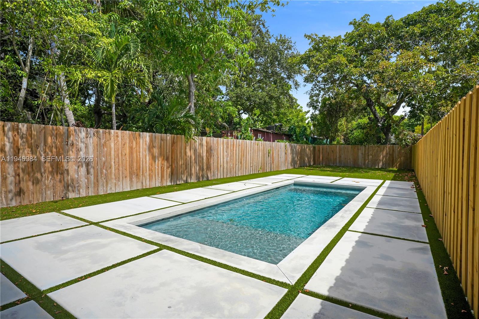 A rectangular swimming pool is surrounded by concrete pavers and artificial turf in a fenced yard — 223 NW 51st St, Miami FL 33127, MIAMI, FL