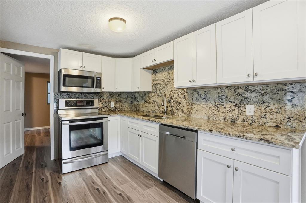 A kitchen features white cabinets, granite countertops, stainless steel appliances, and wood-look flooring — 11311 ALTOONA AVENUE, NEW PORT RICHEY, FL